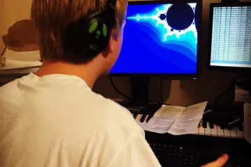 Cade wearing headphones at a desk, with a Mandelbrot rendering on the monitor.